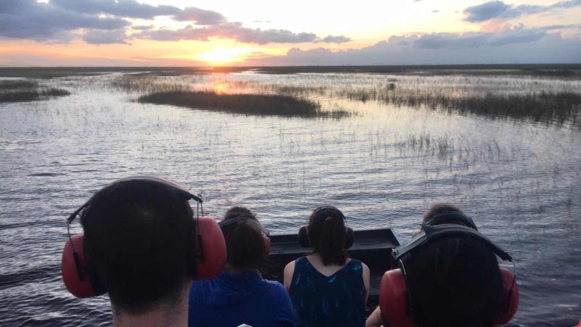 Guests on an Aces airboat watching the sunset over the Everglades marsh