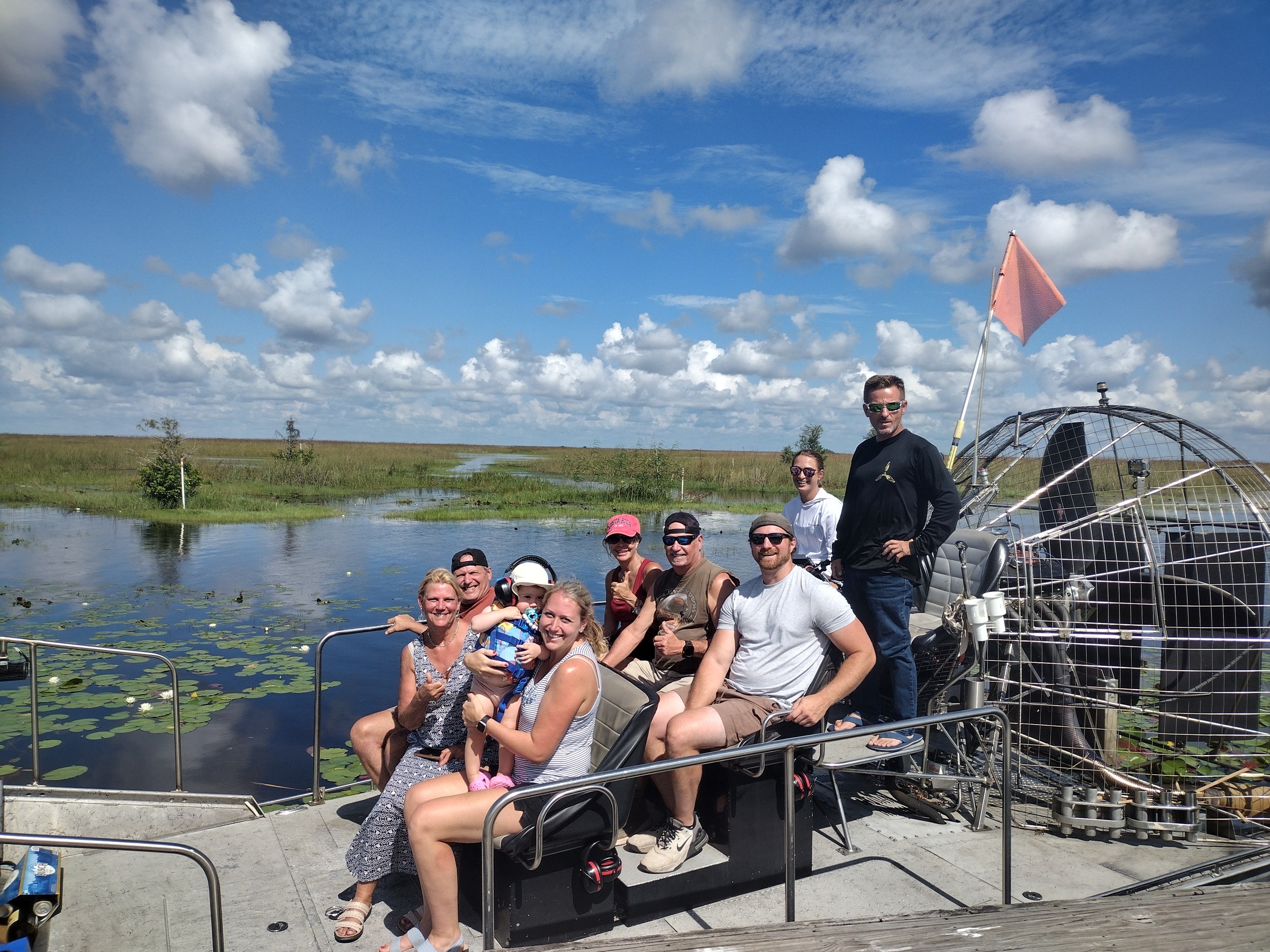 A large group of guests aboard an Aces airboat under a bright blue Everglades sky