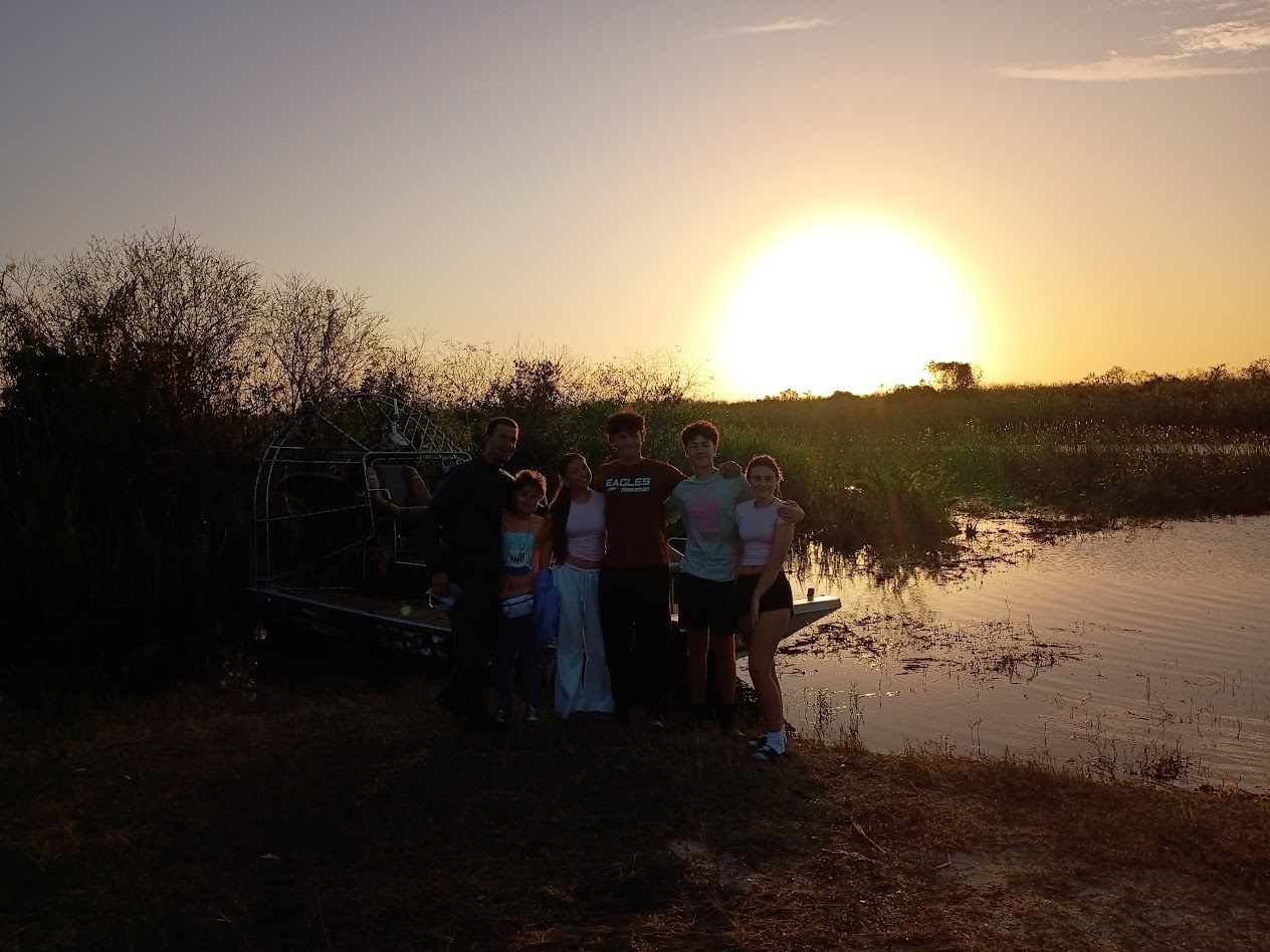 A group of guests posing in front of an Aces airboat at sunset in the Everglades